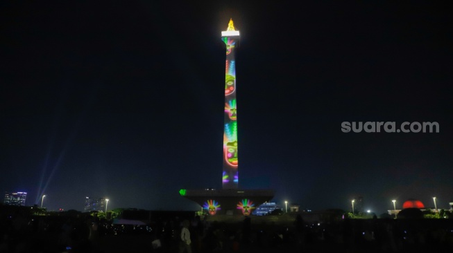 Pengunjung menyaksikan pertunjukan video mapping Monas Week di Monumen Nasional (Monas), Jakarta, Jumat (29/12/2023). [Suara.com/Alfian Winanto]