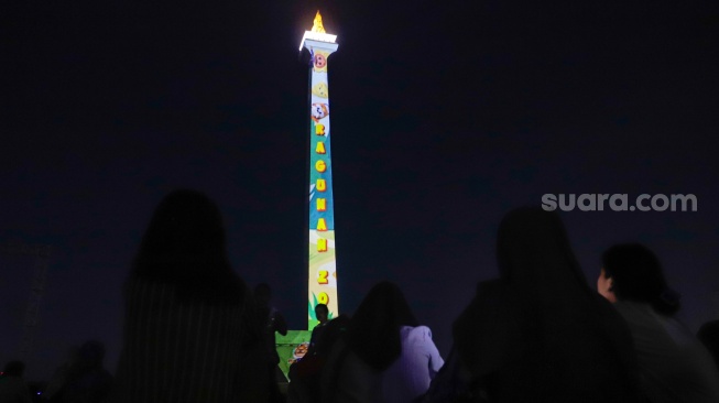 Pengunjung menyaksikan pertunjukan video mapping Monas Week di Monumen Nasional (Monas), Jakarta, Jumat (29/12/2023). [Suara.com/Alfian Winanto]