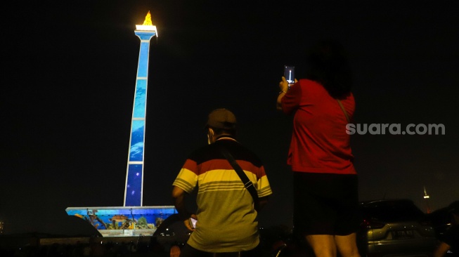 Pengunjung menyaksikan pertunjukan video mapping Monas Week di Monumen Nasional (Monas), Jakarta, Jumat (29/12/2023). [Suara.com/Alfian Winanto]