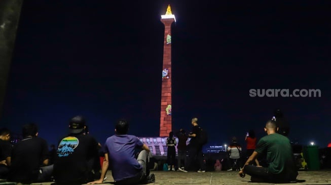 Pengunjung menyaksikan pertunjukan video mapping Monas Week di Monumen Nasional (Monas), Jakarta, Jumat (29/12/2023). [Suara.com/Alfian Winanto]