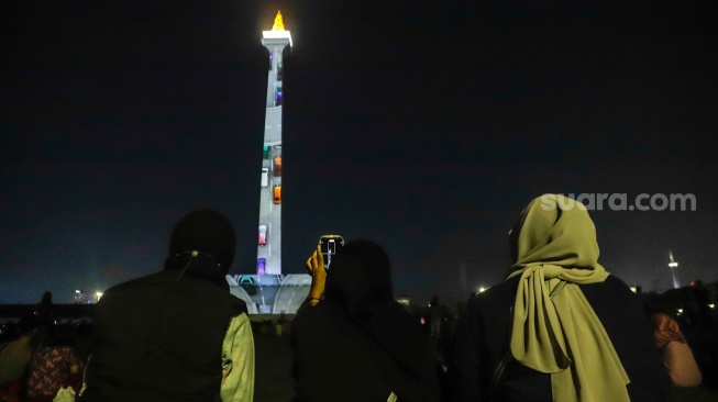 Pengunjung menyaksikan pertunjukan video mapping Monas Week di Monumen Nasional (Monas), Jakarta, Jumat (29/12/2023). [Suara.com/Alfian Winanto]