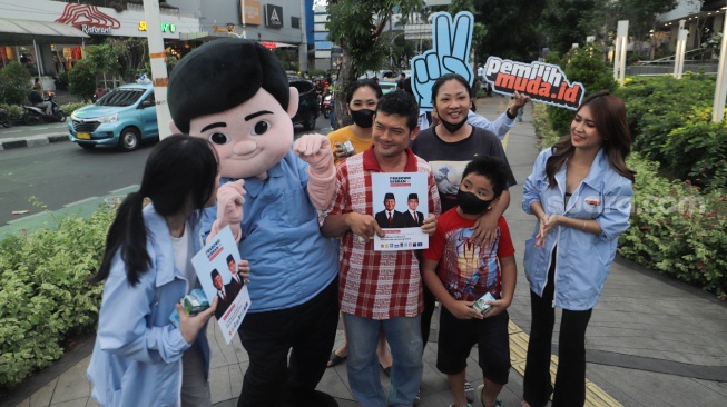 Boneka Gemoy Prabowo Subianto membagikan susu gratis kepada warga yang melintas di Perempatan Lampu Merah Sarinah, Jakarta, Jumat (29/12/2023). [Suara.com/Alfian Winanto]