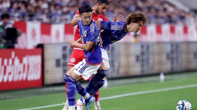 Ko Itakura (kanan) dan Yukinari Sugawara (kiri) dari Jepang berebut bola bersama Elies Ashley dari Tunisia saat pertandingan persahabatan internasional antara Jepang vs Tunisia di Stadion Noevir di Kobe pada 17 Oktober 2023. PAUL MILLER / AFP.