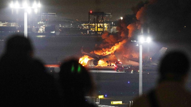 Orang-orang di dek observasi memandangi pesawat Japan Airlines yang terbakar di landasan Bandara Haneda, Tokyo, Jepang, Selasa (2/1/2024). [JIJI PRESS / AFP]