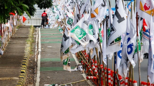 Warga melintas di samping alat peraga kampanye (APK) pemilu 2024 yang terpasang di pembatas jalur sepeda (stick cone) di kawasan Menteng, Jakarta, Selasa (9/1/2024). [Suara.com/Alfian Winanto]