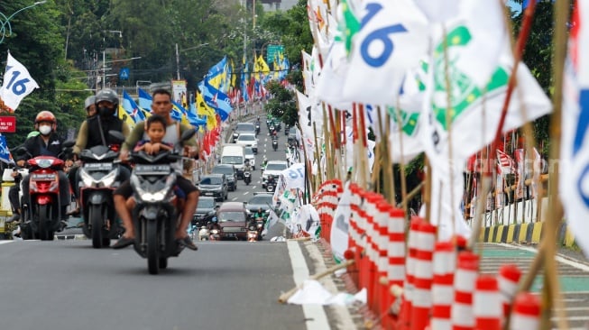 Warga melintas di samping alat peraga kampanye (APK) pemilu 2024 yang terpasang di pembatas jalur sepeda (stick cone) di kawasan Menteng, Jakarta, Selasa (9/1/2024). [Suara.com/Alfian Winanto]