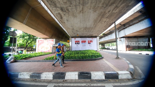 Warga melintas di samping baliho sosialisasi visi dan misi tiga pasangan calon presiden dan wakil presiden 2024 yang terpasang di kawasan Kuningan, Jakarta, Selasa (9/1/2024). [Suara.com/Alfian Winanto]