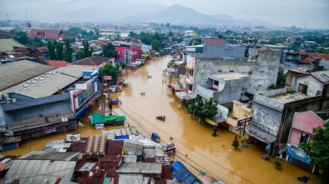 Warga berjalan melewati genangan banjir di Dayeuhkolot, Kabupaten Bandung, Jawa Barat, Jumat (12/1/2024). [Suara.com/Alfian Winanto]