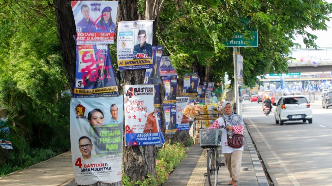 Sejumlah alat peraga kampanye (APK) yang dipaku di pohon dilabeli oleh sekelompok orang dengan cat pilok di Jalan Yos Sudarso, Jakarta Utara, Sabtu (13/1/2024). [Suara.com/Alfian Winanto]