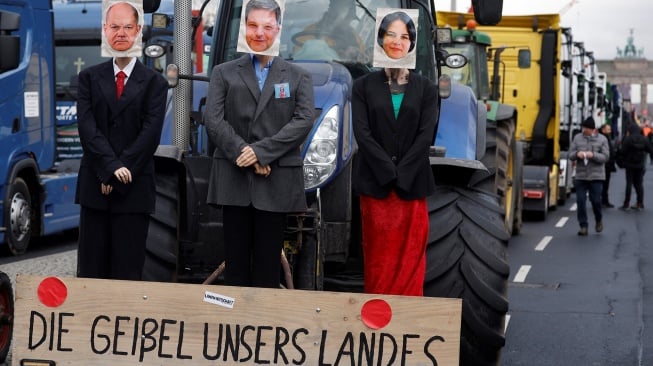 Sebuah traktor dihiasi dengan boneka bergambar Kanselir Jerman Olaf Scholz, Menteri Ekonomi dan Perlindungan Iklim Jerman Robert Habeck dan Menteri Luar Negeri Jerman Annalena Baerbock dan sebuah plakat bertuliskan 'Momok negara kita' terlihat saat saksi protes para petani dan pengemudi truk di Berlin, Jerman, Senin (15/1/2024). [Odd ANDERSEN / AFP] 