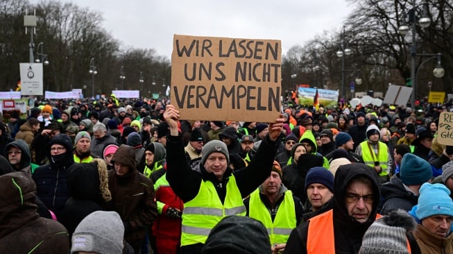 Seorang pengunjuk rasa mengacungkan plakat berisi tuntutan saat aksi protes para petani dan pengemudi truk di Berlin, Jerman, Senin (15/1/2024). [JOHN MACDOUGALL / AFP] 