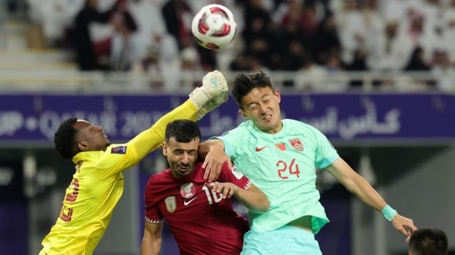 Penjaga gawang timnas Qatar #22 Meshaal Barsham melompat untuk meninju bola saat beknya #16 Boualem Khoukhi dan bek China #24 Jiang Shenglong bersaing selama pertandingan terakhir Grup A Piala Asia 2023 antara Qatar vs China di Stadion Internasional Khalifa di Doha pada 22 Januari 2024.Giuseppe CACACE / AFP