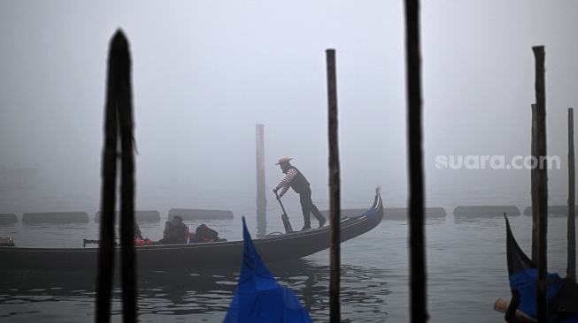 Sebuah gondola berlayar di tengah kabut saat pra-pembukaan karnaval di Venesia, Italia, Sabtu (27/1/2024). [GABRIEL BOUYS / AFP] 