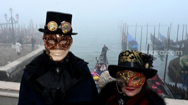 Seorang pengunjung mengenakan topeng dan kostum kuno berpose saat pra-pembukaan karnaval di Venesia, Italia, Sabtu (27/1/2024). [GABRIEL BOUYS / AFP] ​ 