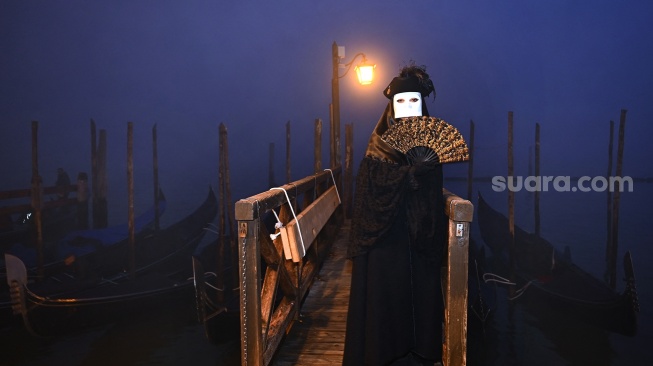 Seorang pengunjung mengenakan topeng dan kostum kuno berpose saat pra-pembukaan karnaval di Venesia, Italia, Sabtu (27/1/2024). [GABRIEL BOUYS / AFP] ​ 