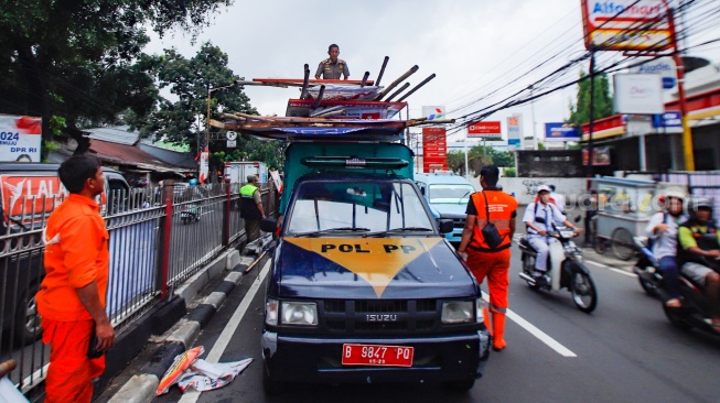 Petugas membongkar Alat Peraga Kampanye (APK) yang terpasang di Kawasan Kramat Jati, Jakarta, Senin (29/1/2024). [Suara.com/Alfian Winanto]