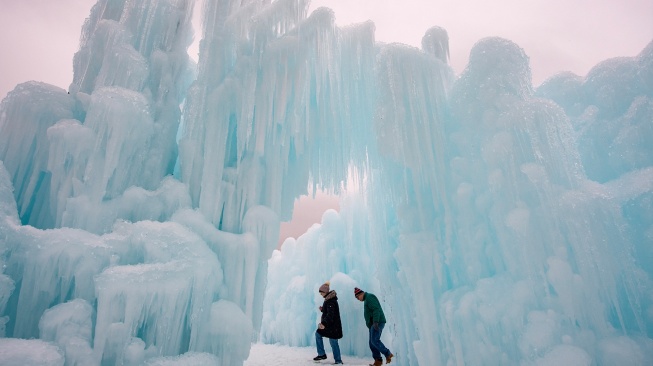 Orang-orang menjelajahi dinding es, jalan setapak, dan gua di Ice Castles di North Woodstock, New Hampshire, Amerika Serikat, Kamis (1/2/2024). [Joseph Prezioso / AFP]