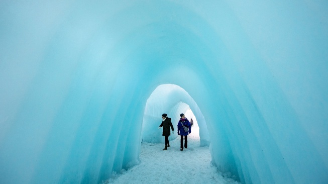 Orang-orang menjelajahi dinding es, jalan setapak, dan gua di Ice Castles di North Woodstock, New Hampshire, Amerika Serikat, Kamis (1/2/2024). [Joseph Prezioso / AFP]