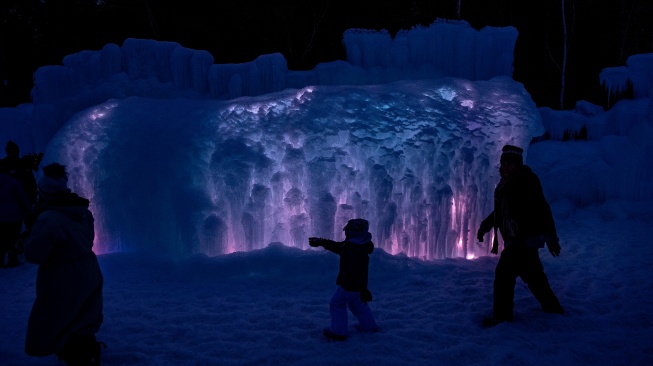 Orang-orang berjalan melewati dinding es yang diterangi cahaya di Ice Castles di North Woodstock, New Hampshire, Amerika Serikat, Kamis (1/2/2024). [Joseph Prezioso / AFP]
