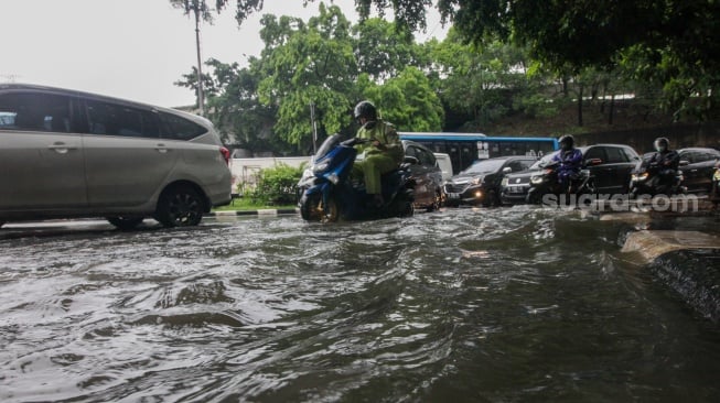 Kendaraan melintasi genangan banjir di Jalan DI Panjaitan, Jakarta, Senin (5/2/2024). [Suara.com/Alfian Winanto]