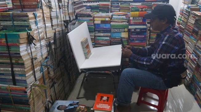 Pedagang memfoto buku dagangannya untuk dijual secara online di Sentra Buku Pasar Kenari, Jakarta, Senin (5/2/2024). [Suara.com/Alfian Winanto]