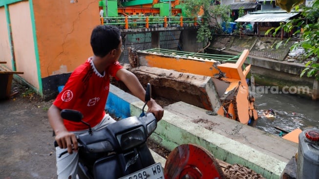 Warga melihat pos pantau Pintu Air Palmerah yang rubuh di Palmerah, Jakarta, Selasa (6/2/2024). [Suara.com/Alfian Winanto]