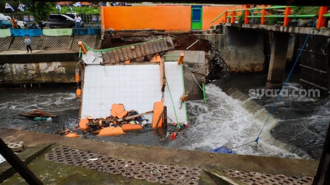 Warga melihat pos pantau Pintu Air Palmerah yang rubuh di Palmerah, Jakarta, Selasa (6/2/2024). [Suara.com/Alfian Winanto]