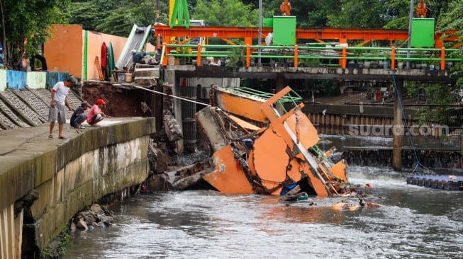 Warga melihat pos pantau Pintu Air Palmerah yang rubuh di Palmerah, Jakarta, Selasa (6/2/2024). [Suara.com/Alfian Winanto]