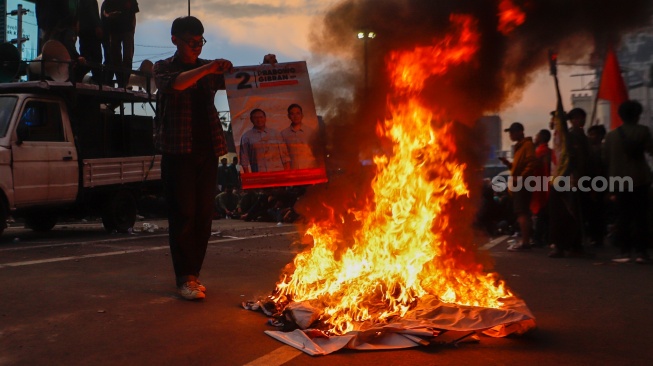 Seorang mahasiswa membakar poster salah satu capres saat menggelar aksi unjuk rasa di belakang Istana Negara, Jakarta, Rabu (7/2/2024). [Suara.com/Alfian Winanto]