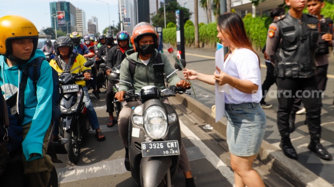 Sejumlah aktivis membagikan bunga mawar ke pengendara motor saat menggelar aksi di kawasan Bundaran Hotel Indonesia (HI), Jakarta, Selasa (13/2/2024). [Suara.com/Alfian Winanto]