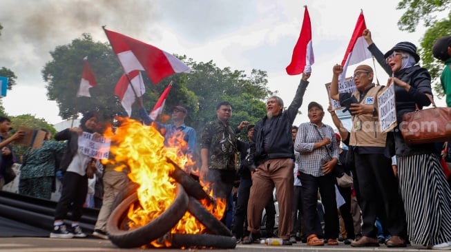 Massa yang tergabung dalam Gerakan Masyarakat Sipil Selamatkan Demokrasi Indonesia membakar ban saat menggelar aksi di depan Gedung Komisi Pemilihan Umum (KPU) RI, Jakarta, Jumat (23/2/2024). [Suara.com/Alfian Winanto]