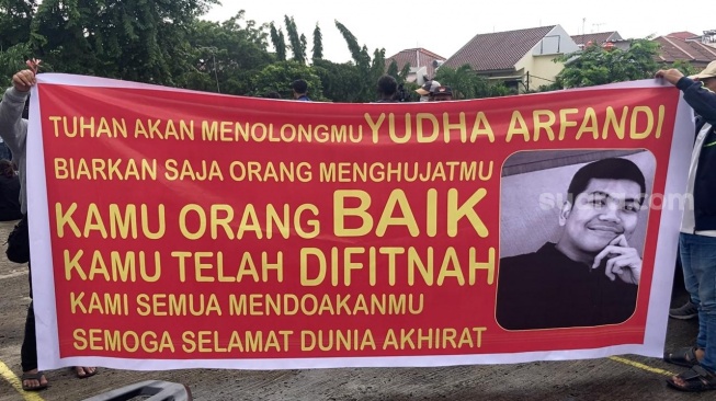 Keluarga tersangka Yudha Arfandi bawa spanduk ke lokasi rekonstruksi kematian Dante di kolam renang Taman Air Tirtamas, Pondok Kelapa, Jakarta, Rabu (28/2/2024) [Suara.com/Adiyoga Priyambodo]