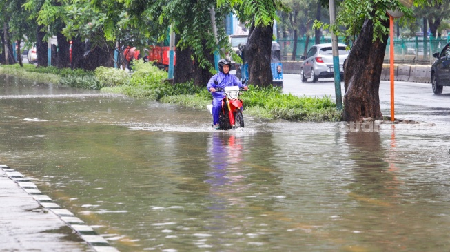 Seorang pengendara motor melintas banjir di sekitar Cempaka Putih, Jakarta, Kamis (29/2/2024). [Suara.com/Alfian Winanto]