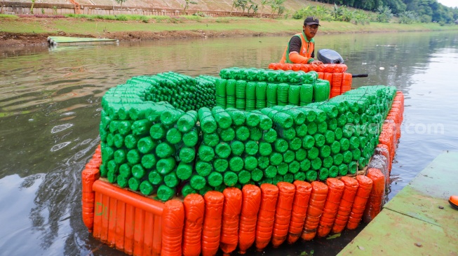 Petugas UPS Badan Air Dinas Lingkungan Hidup DKI Jakarta menaiki perahu motor berbahan botol plastik bekas di Kanal Banjir Timur, Duren Sawit, Jakarta, Rabu (6/3/2024). [Suara.com/Alfian Winanto]