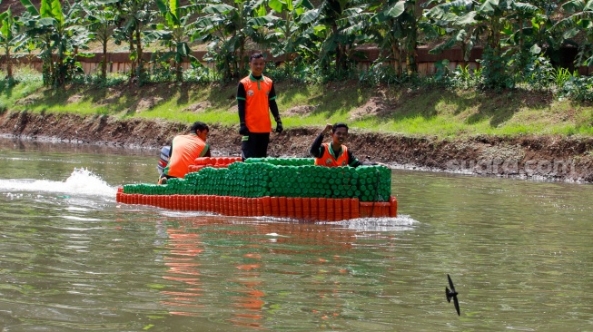 Petugas UPS Badan Air Dinas Lingkungan Hidup DKI Jakarta menaiki perahu motor berbahan botol plastik bekas di Kanal Banjir Timur, Duren Sawit, Jakarta, Rabu (6/3/2024). [Suara.com/Alfian Winanto]