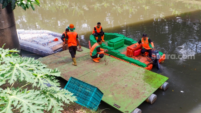 Petugas UPS Badan Air Dinas Lingkungan Hidup DKI Jakarta mengoperasikan perahu motor berbahan botol plastik bekas di Kanal Banjir Timur, Duren Sawit, Jakarta, Rabu (6/3/2024). [Suara.com/Alfian Winanto]