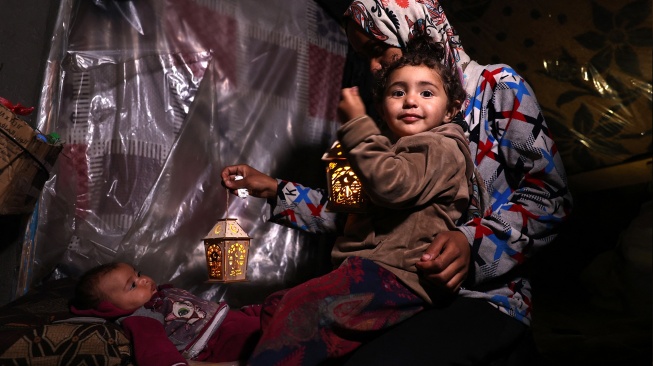 Anak-anak Palestina bermain dengan lentera tradisional "fanous" menyambut dimulainya bulan suci Ramadhan, di kota Rafah, Jalur Gaza selatan, Palestina, Minggu (10/3/2024). [SAID KHATIB/AFP]
