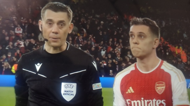 Potret winger Arsenal, Leandro Trossard (kanan) dan wasit Clement Turpin dalam laga Arsenal vs Porto di leg kedua babak 16 besar Liga Champions 2023-2024 di Stadion Emirates, London, Rab (13/3/2024) dini hari WIB. Kedua sosok dianggap punya wajah mirip hingga banyak fans yang menuding mereka punya hubungan darah. [Dok. X/@nocontextfooty]