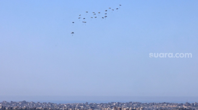 Gambar yang diambil dari perbatasan selatan Israel dengan Jalur Gaza ini menunjukkan bantuan kemanusiaan dijatuhkan dari udara di wilayah Palestina pada Selasa (12/3/2024).  [Menahem KAHANA/AFP] 