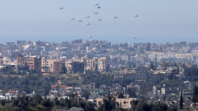 Gambar yang diambil dari perbatasan selatan Israel dengan Jalur Gaza ini menunjukkan bantuan kemanusiaan dijatuhkan dari udara di wilayah Palestina pada Selasa (12/3/2024).  [Menahem KAHANA/AFP] 