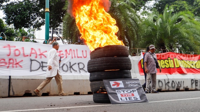 Massa yang tergabung dalam Gerakan Masyarakat Sipil Selamatkan Demokrasi Indonesia membakar ban saat menggelar aksi di depan Gedung Komisi Pemilihan Umum (KPU) RI, Jakarta,  Senin (18/3/2024). [Suara.com/Alfian Winanto]