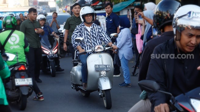 Capres nomor urut satu, Anies Baswedan menyapa warga saat mengendarai Vespa usai membeli Takjil untuk berbuka puasa di Pasar Takjil Benhil, Jakarta, Rabu (20/3/2024). [Suara.com/Alfian Winanto]