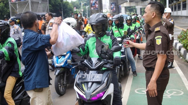 Petugas membagikan paket bantuan bahan pangan di depan Gedung Kejaksaan Agung RI, Jakarta, Senin (1/4/2024). [Suara.com/Alfian Winanto]