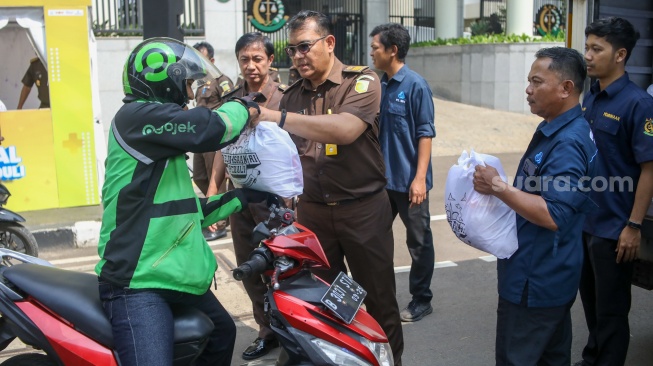 Petugas membagikan paket bantuan bahan pangan di depan Gedung Kejaksaan Agung RI, Jakarta, Senin (1/4/2024). [Suara.com/Alfian Winanto]