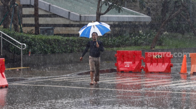 Warga berjalan menggunakan payung saat turun hujan di Kawasan Dukuh Atas, Jakarta, Rabu (3/4/2024). [Suara.com/Alfian Winanto]