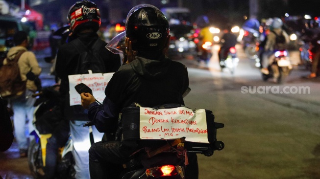 Kertas berisi pesan - pesan terpasang di belakang kendaraan pemudik bersepeda motor yang melintas di Jalan Inspeksi Kalimalang, Jakarta, Sabtu (6/4/2024). [Suara.com/Alfian Winanto]