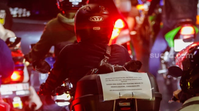 Kertas berisi pesan - pesan terpasang di belakang kendaraan pemudik bersepeda motor yang melintas di Jalan Inspeksi Kalimalang, Jakarta, Sabtu (6/4/2024). [Suara.com/Alfian Winanto]