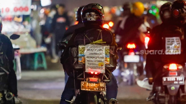 Kertas berisi pesan - pesan terpasang di belakang kendaraan pemudik bersepeda motor yang melintas di Jalan Inspeksi Kalimalang, Jakarta, Sabtu (6/4/2024). [Suara.com/Alfian Winanto]