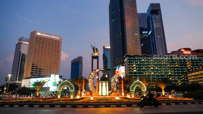 Sejumlah kendaraan melintas di depan dekorasi lebaran di kawasan Bundaran Hotel Indonesia, Jakarta, Senin (8/4/2024). [Suara.com/Alfian Winanto]