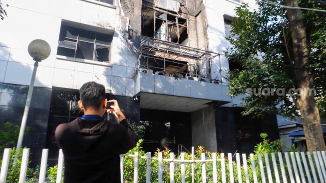 Seorang Jurnalis mengambil gambar gedung YLBHI yang terbakar di Menteng, Jakarta, Senin (8/4/2024). [Suara.com/Alfian Winanto]